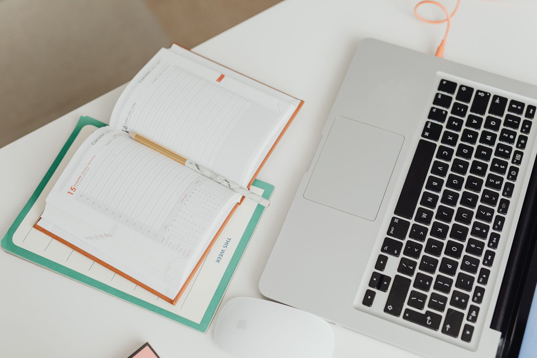 Top view of a clean workspace with a laptop, notebook, and mouse on a desk.