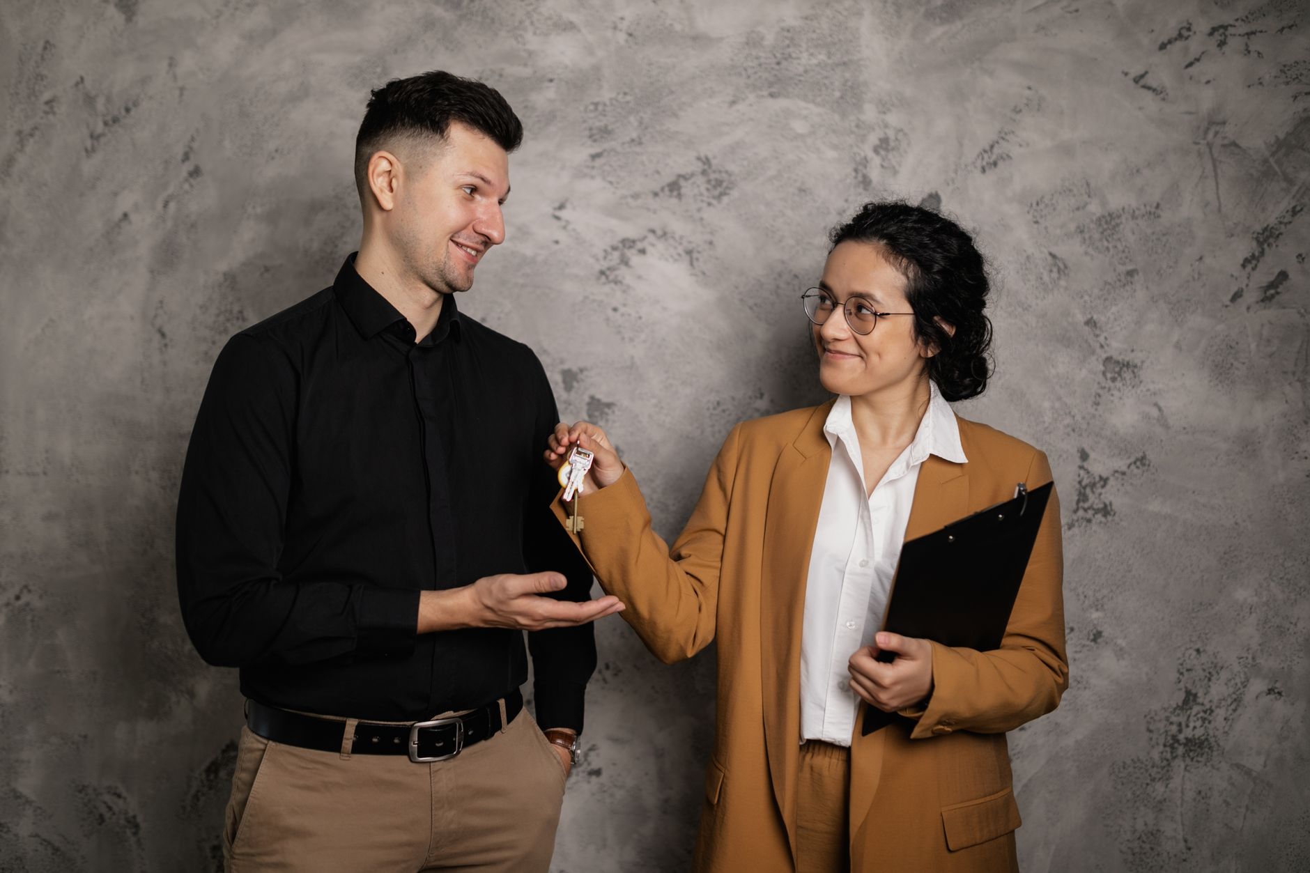 A real estate agent smiling as they hand over house keys to a new homeowner in an indoor setting.