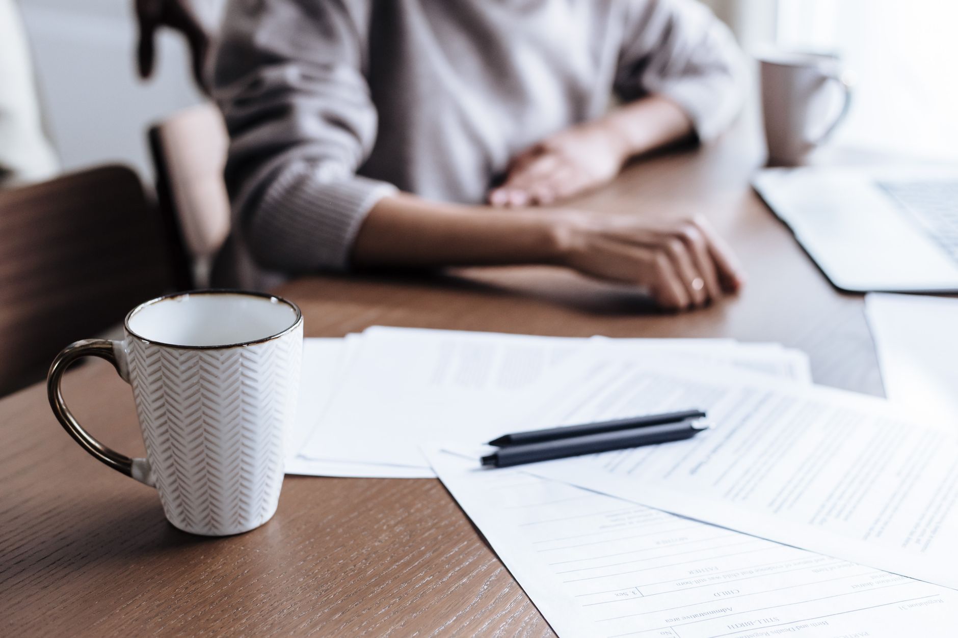 Close-up of a woman working from home, focusing on documents and a coffee mug.